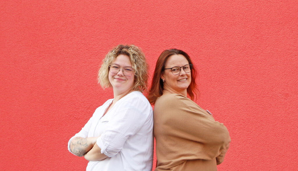 Katja Gutmann (r.) und Daniela Geißler (l.) vor einer roten Wand.